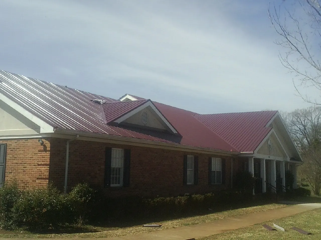 Red metal roof with gabled entries on a long brick building, from a Hail Damage Roof Repair job in Schenectady