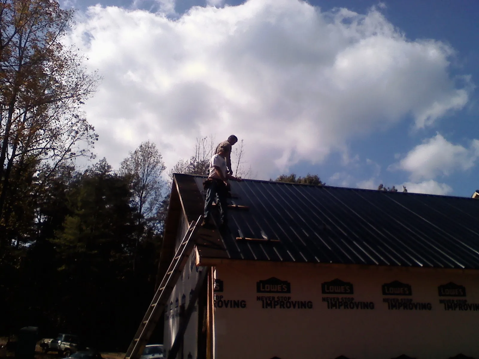 Roofer fastening dark metal panels high against a cloudy sky, from a Roof Inspection job in Schenectady