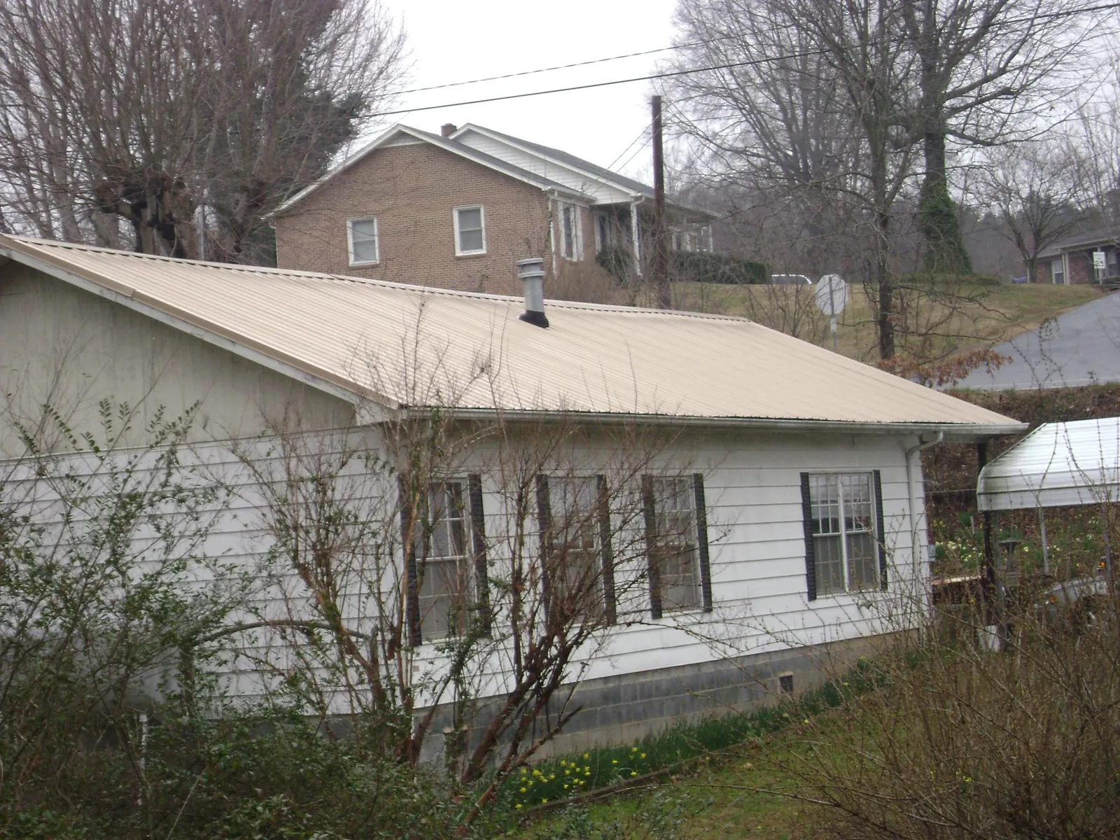 Tan metal roof on a white sided house set into a hillside — Commercial Roofing by Roofing Brothers in Schenectady